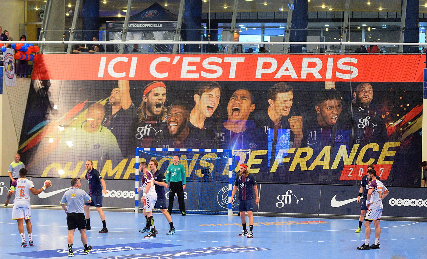 Joueurs du PSG et du HBC Nantes sur le terrain de Coubertin, devant une tribune parisienne.